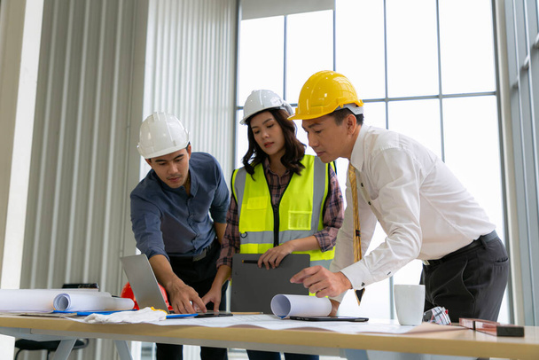 Mühendislerden oluşan bir takım mimar çalışma masasında duruyor ve inşaat planları üzerinde çalışıyor. Mühendisler konuşuyor. - Fotoğraf, Görsel