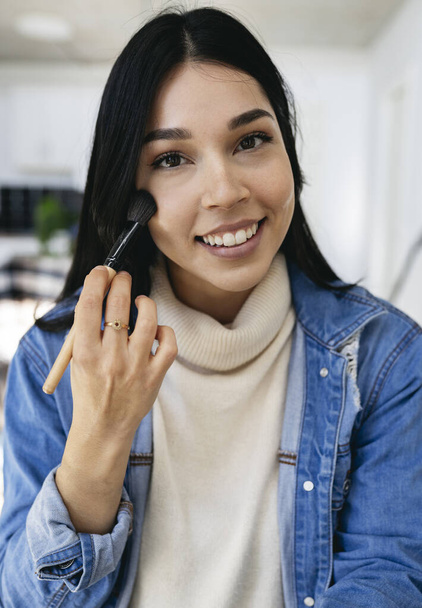 vertical photo of a pretty Hispanic woman putting on makeup at home - Foto, imagen