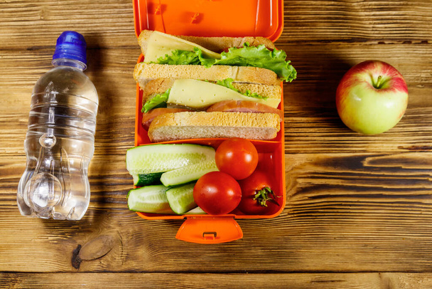 Lahvička s vodou, jablkem a občerstvením se sendviči a čerstvou zeleninou na dřevěném stole. Horní pohled - Fotografie, Obrázek