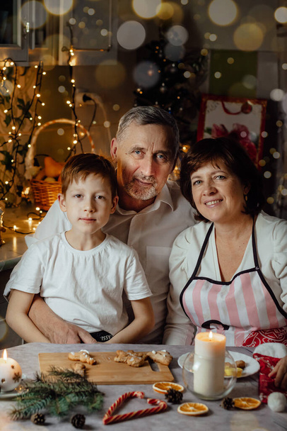 Karácsonyi party boldog család a konyhában, gyermek fiú ül együtt nagymama és nagyapa néz a kamera, függőleges fotó - Fotó, kép