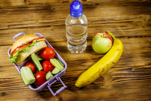 Bir şişe su, elma, muz ve hamburgerli beslenme çantası ve ahşap bir masada taze sebze. - Fotoğraf, Görsel