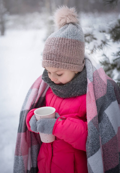 Petite fille enveloppée dans une couverture buvant du thé dans la forêt d'hiver - Photo, image