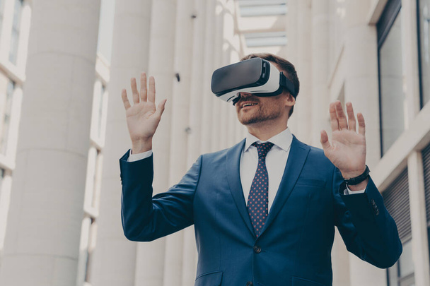 Бізнесмен, використовуючи гарнітуру VR для гри віртуальної реальності для роботи, стоїть на відкритому повітрі
 - Фото, зображення