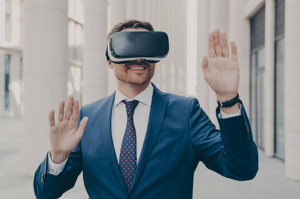 Biznesmen w garniturze próbuje i doświadcza wirtualnej rzeczywistości za pomocą mobilnych gogli VR na zewnątrz - Zdjęcie, obraz