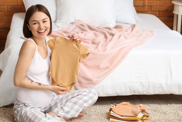 Young pregnant woman with baby bodysuit in bedroom - Photo, Image