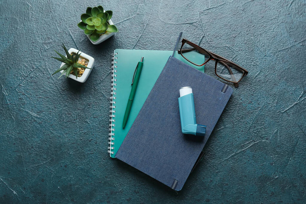 Inhalator astmy, zeszyty, długopisy, okulary i roślina domowa na ciemnym tle - Zdjęcie, obraz