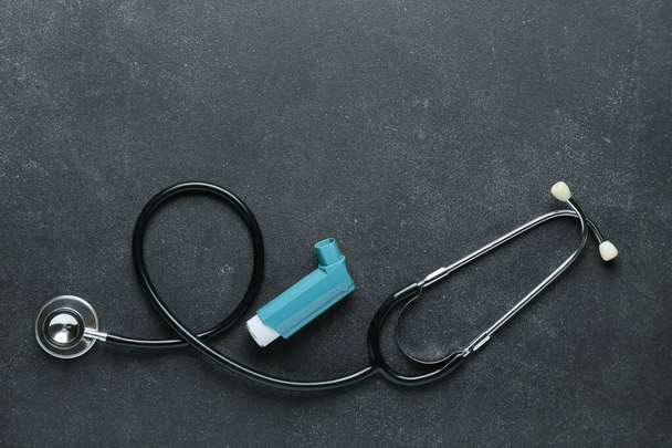 Astma-inhalator en stethoscoop op donkere achtergrond - Foto, afbeelding