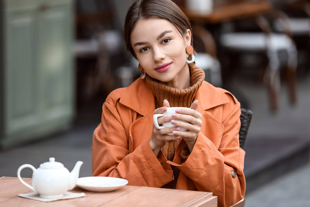 Portrait de belle jeune femme tenant une tasse de thé chaud dans un café de rue - Photo, image