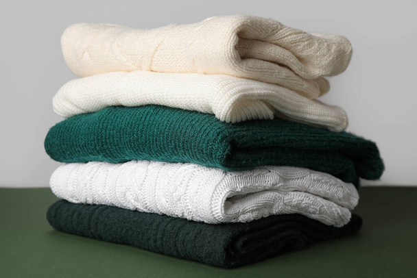 Стек стильних в'язаних светрів на зеленому столі на сірому фоні
 - Фото, зображення