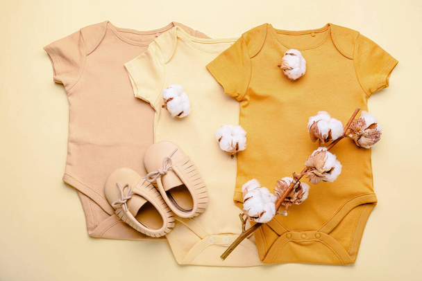 Set van baby bodysuits, schoenen en katoen tak op kleur achtergrond - Foto, afbeelding