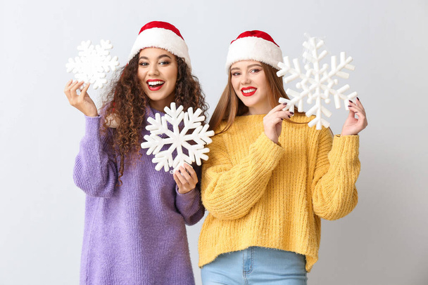 Schöne junge Frauen in Weihnachtsmützen und mit Schneeflocken auf hellem Hintergrund - Foto, Bild