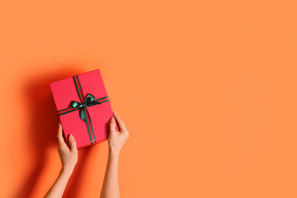 Γυναικεία χέρια με όμορφο κουτί δώρου Χριστουγέννων σε πορτοκαλί φόντο - Φωτογραφία, εικόνα