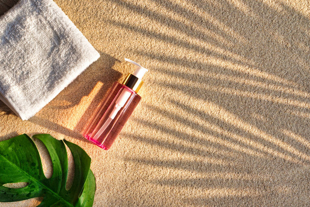 Cosmetic moisturizer, oil or serum bottle in beach sand next to palm leaves and straw hat. Natural cosmetics, sunscreen cosmetics concept. Close up. - Photo, Image
