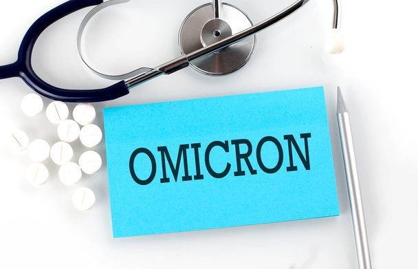 Szöveg OMICRON az asztalon sztetoszkóppal, tabletták és toll, orvosi koncepció. - Fotó, kép
