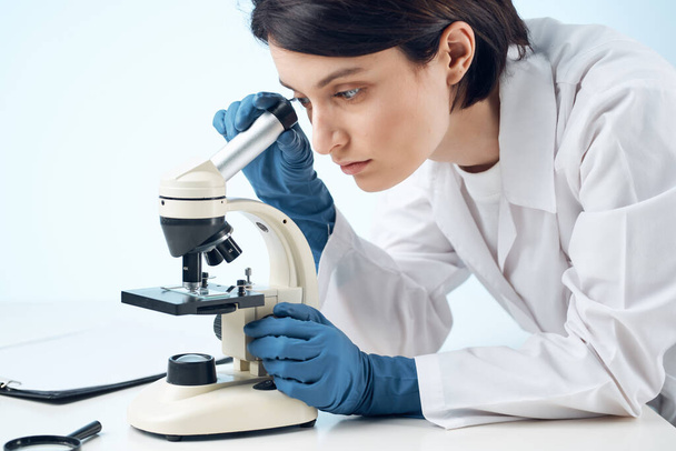medico donna seduto a tavola microscopio ricerca biotecnologia luce sfondo - Foto, immagini