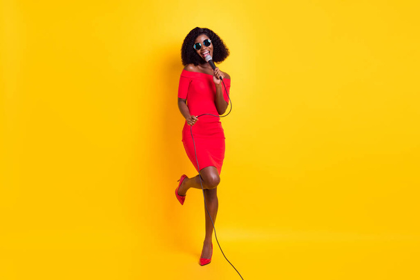 Full size photo of young beautiful gorgeous happy afro girl in sunglasses singing karaoke isolated on yellow color background - Valokuva, kuva