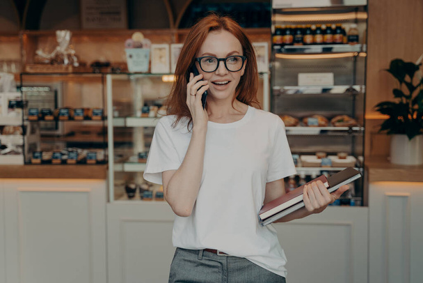 Πολυσύχναστη γυναίκα ιδιοκτήτης αρτοποιείου έχει συνομιλία στο κινητό τηλέφωνο - Φωτογραφία, εικόνα