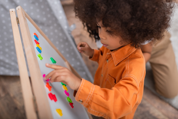 High angle view of african american child playing with signs on magnetic board near mom at home  - Photo, Image