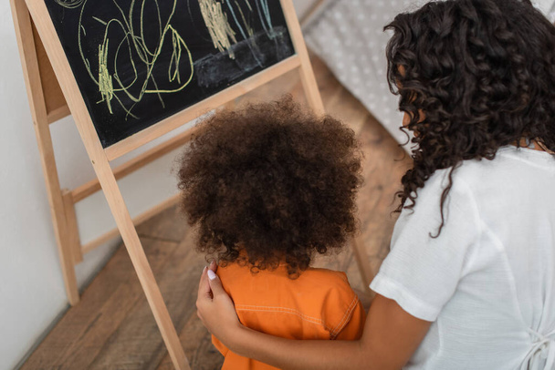 Overhead view of african american woman hugging child near chalkboard at home  - Fotografie, Obrázek