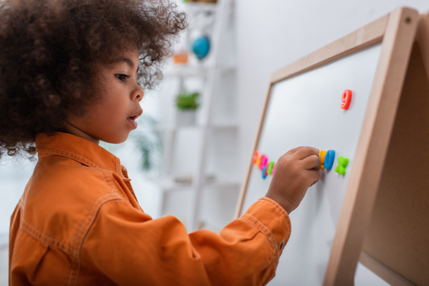 Side view of african american kid applying signs on magnetic board at home  - Foto, immagini