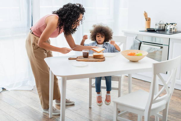 African american parent holding knife and bread near daughter and chocolate paste at home  - Fotoğraf, Görsel