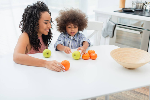 Улыбающаяся африканская американская мама держит оранжевый рядом с дочерью на кухне  - Фото, изображение