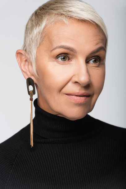 pleased senior woman with long earring and black turtleneck isolated on grey - Fotó, kép