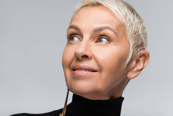 smiling senior woman with long earring and black turtleneck isolated on grey - Фото, зображення