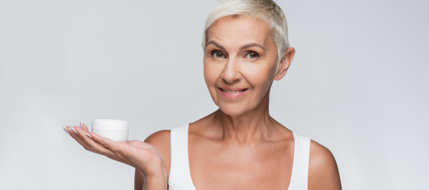 happy senior woman holding container with face cream isolated on grey, banner - Φωτογραφία, εικόνα