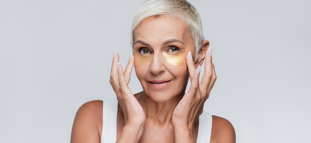 smiling senior woman applying collagen eye patches isolated on grey, banner - Foto, Imagem