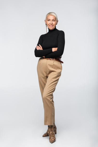 longitud completa de mujer mayor complacida y de moda posando con los brazos cruzados en gris - Foto, Imagen