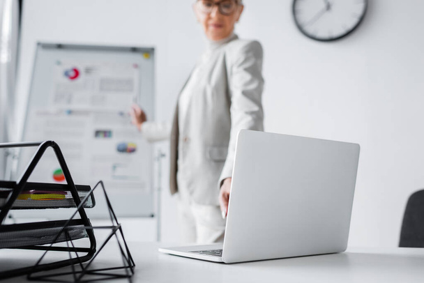 laptop on desk near blurred businesswoman in office  - Fotó, kép