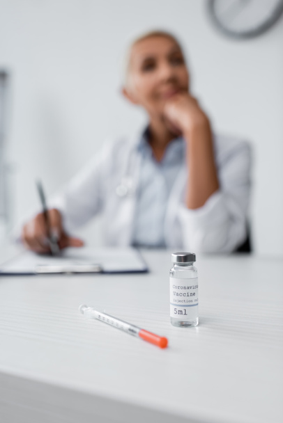 bottle with coronavirus vaccine near syringe and blurred doctor on background - Фото, зображення
