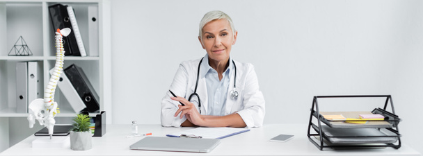 smiling doctor holding pen near devices on desk, banner - Foto, immagini
