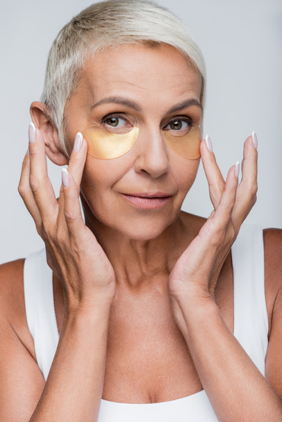 portrait of senior woman applying collagen eye patches isolated on gray - Zdjęcie, obraz