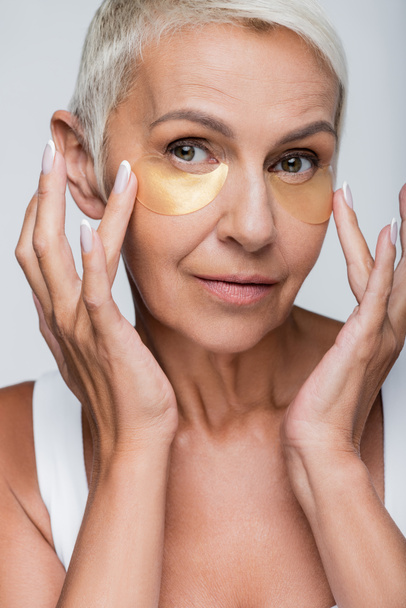 portrait of senior woman applying eye patches isolated on grey - Foto, Bild
