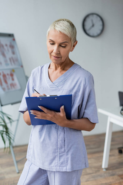 doctor with grey hair standing and writing prescription in clipboard  - Foto, imagen