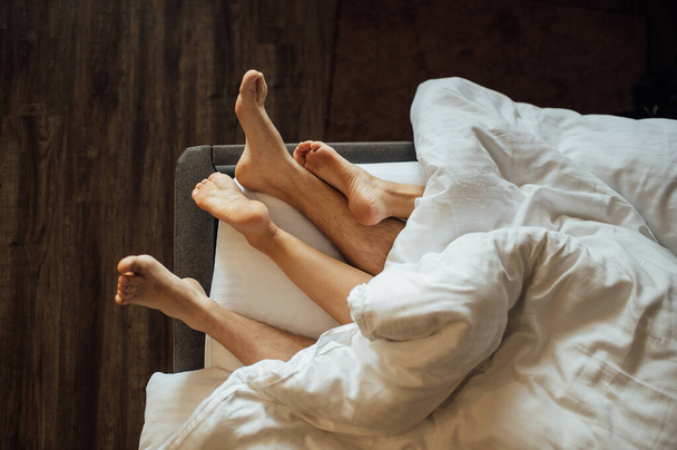 The feet of a young heterosexual couple relaxing in bed. - Фото, изображение