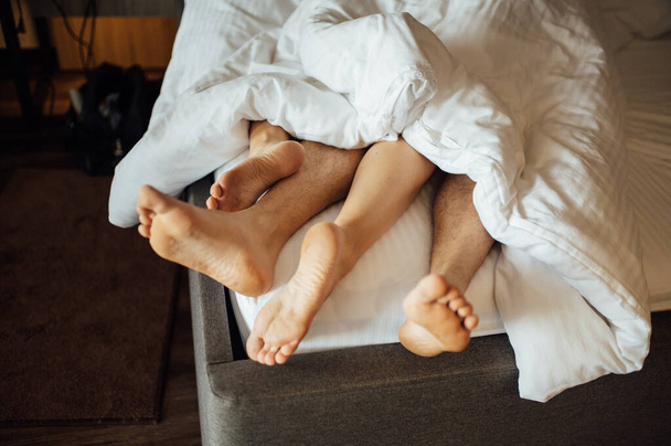 Die Füße eines jungen heterosexuellen Paares entspannen sich im Bett. - Foto, Bild