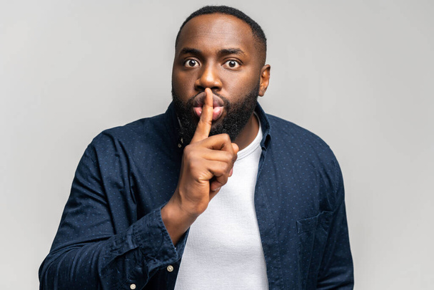 African-American guy holding index finger near lips in shh gesture - Фото, изображение