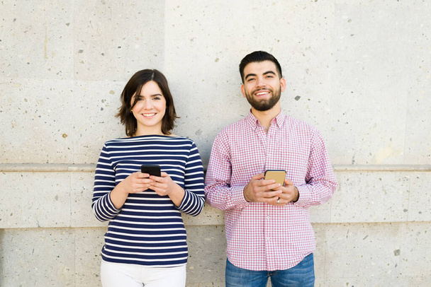 Heureux couple caucasien faisant un contact visuel et souriant tout en envoyant des SMS sur leurs smartphones lors d'une date  - Photo, image