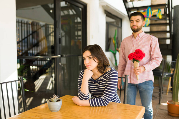 I'm sorry I'm late. Young man bringing flowers to her angry girlfriend waiting at a coffee shop - Photo, Image