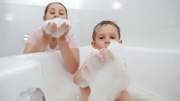 Positive smiling boy with mother playing and having fun with soap foam in bath. Concept of family time, children development and fun at home - Footage, Video