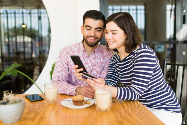 Heyecanlı çift akıllı telefondan online alışveriş yapıyor ve kafede kredi kartıyla ödeme yapıyor.  - Fotoğraf, Görsel