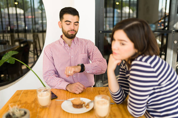 Mislukt afspraakje. verontwaardigde jongeman kijkend naar de tijd op haar horloge tijdens een saai afspraakje met een vrouw - Foto, afbeelding
