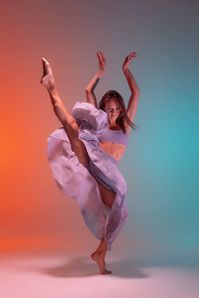Dynamic portrait of young flexible contemp dancer dancing isolated on gradient blue orange background in neon. - Fotografie, Obrázek