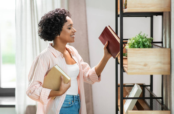 smiling woman arranging books on shelving at home - Photo, Image