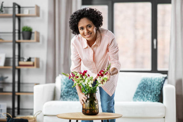 happy woman placing flowers on table at home - Foto, Bild
