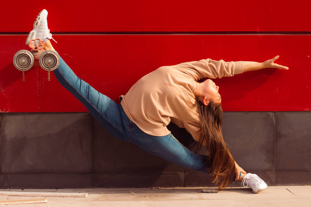 Гимнастка в бечевке на улице на красном фоне, в синих джинсах и бежевом свитере - Фото, изображение