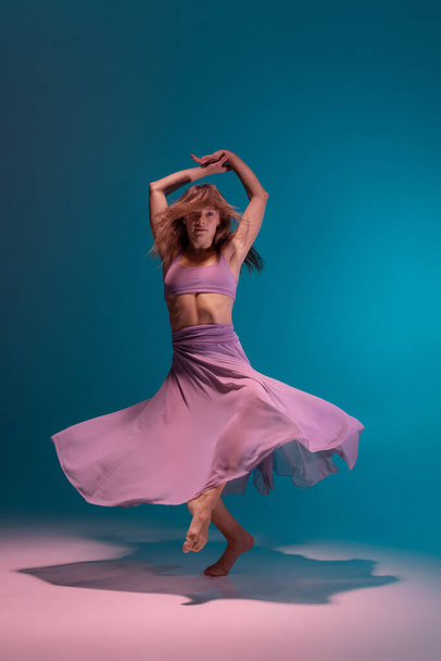 One young flexible contemp dancer in lilac dress dancing isolated on gradient blue white background in neon. - Fotó, kép